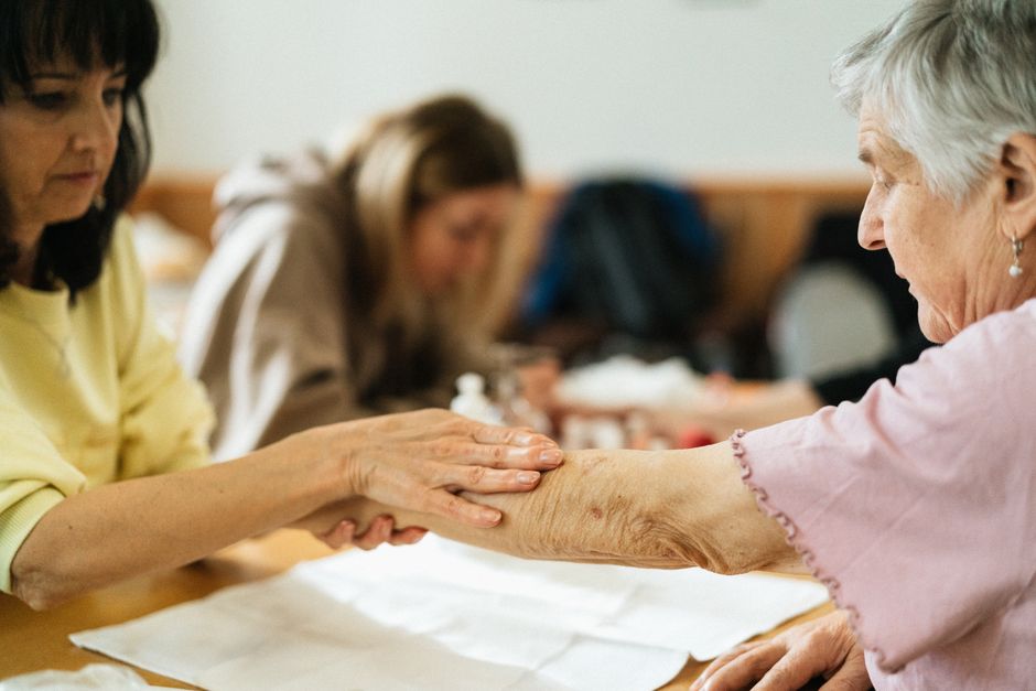 Política nos Bastidores. — A caregiver gently supports an elderly woman's arm during a community activity.
